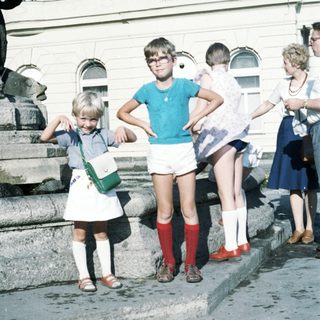 Children posing outdoors near statue, 1970s-80s style clothing.