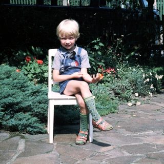 Young child sitting on chair outdoors near garden.