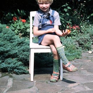 Young child sitting on chair outdoors near garden.