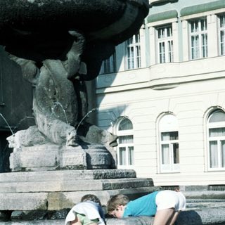 Two children playing near a fountain statue.