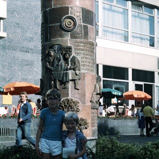 Two children posing near a decorative monument in an urban plaza.