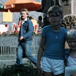 Two children posing near a decorative monument in an urban plaza.