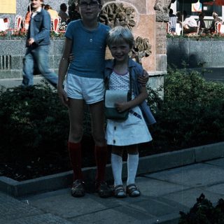 Two children posing near a decorative monument in an urban plaza.