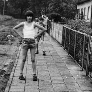 Boy in shorts posing on paved path near trash bins.