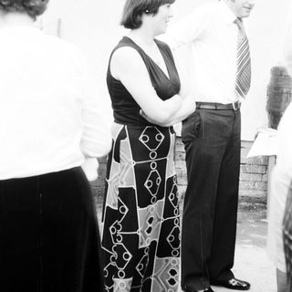 People standing outdoors, man adjusting woman's blouse.