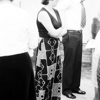 People standing outdoors, man adjusting woman's blouse.