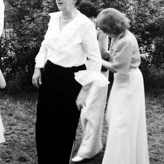 Two women outdoors, one adjusting the other's dress.