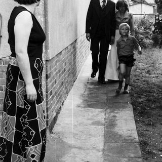 Family walking outside near a house. Woman observing.