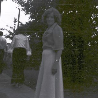 Woman in 1970s-style dress outdoors with trees.