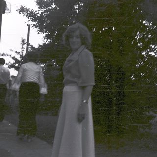 Woman in 1970s-style dress outdoors with trees.
