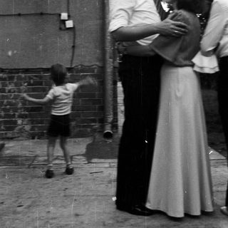 Child playing outside while adults stand nearby.