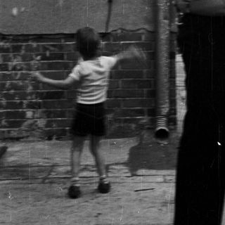 Child playing outside while adults stand nearby.