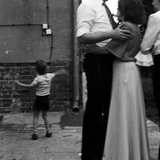 Child playing outside while adults stand nearby.