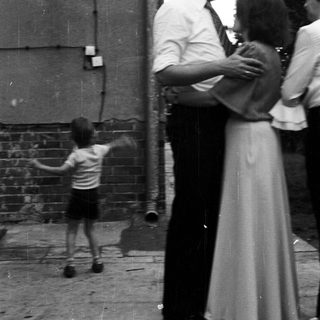 Child playing outside while adults stand nearby.