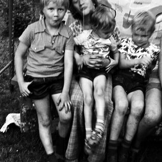 Four children sitting closely outdoors, mid-1980s style.