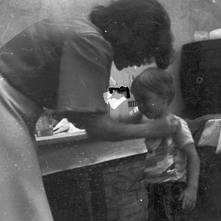 A woman assists a young child at a kitchen sink.