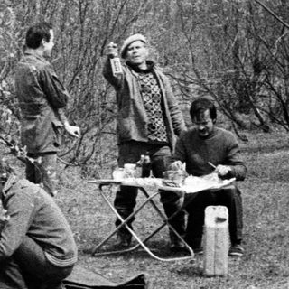 People camping outdoors, preparing food by fire.