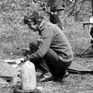 People camping outdoors, preparing food by fire.