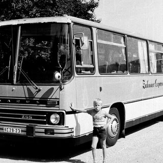 Young boy posing beside vintage coach bus.