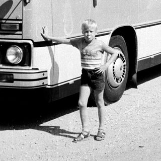 Young boy posing beside vintage coach bus.