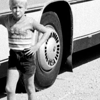 Young boy posing beside vintage coach bus.