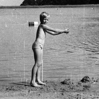 Young boy standing in shallow water near lake.