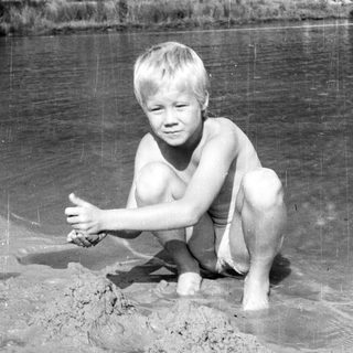 Shirtless boy playing in shallow, muddy water.