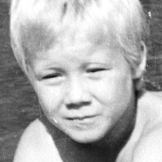Shirtless boy playing in shallow, muddy water.