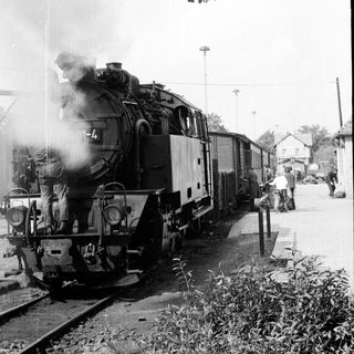 Steam locomotive pulling passenger cars at a station.
