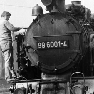 Steam locomotive numbered 99 6001-4 pulling passenger cars.