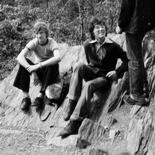 Three people sitting on rocky hillside overlooking forested area.
