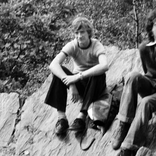Three people sitting on rocky hillside overlooking forested area.