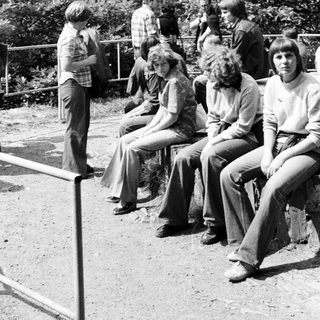 Group of young people sitting outdoors in 1970s-style clothing.