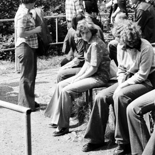 Group of young people sitting outdoors in 1970s-style clothing.