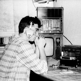 Man using vintage telephone in room with old electronics.