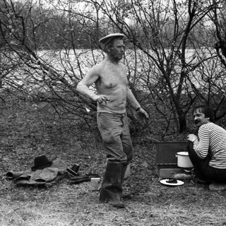 Men camping outdoors, preparing food by fire.