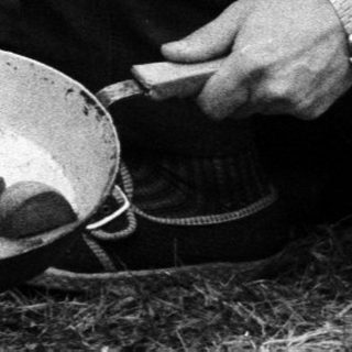 Man cooking fish outdoors over portable stove.
