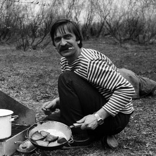 Man cooking fish outdoors over portable stove.