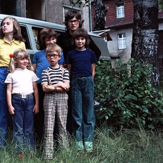 Five children and two adults posing near a vintage Volkswagen van.