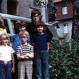 Five children and two adults posing near a vintage Volkswagen van.