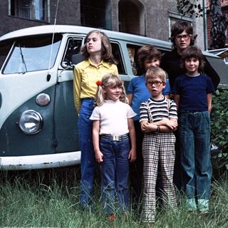 Five children and two adults posing near a vintage Volkswagen van.