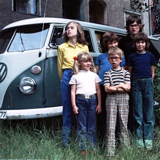 Five children and two adults posing near a vintage Volkswagen van.