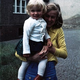 Two people, likely mother and child, smiling outdoors.