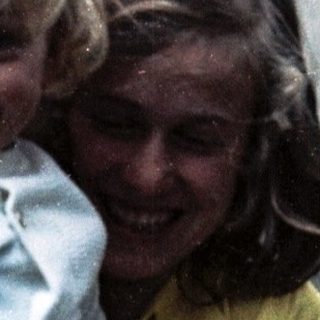 Two people, likely mother and child, smiling outdoors.