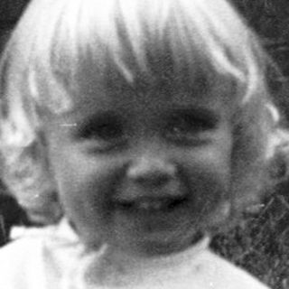 Young child smiling in grassy outdoor area.