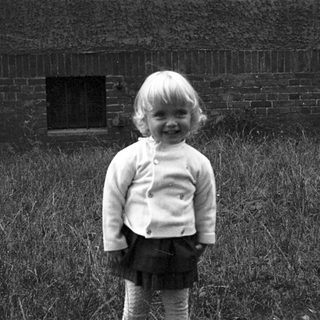 Young child smiling in grassy outdoor area.