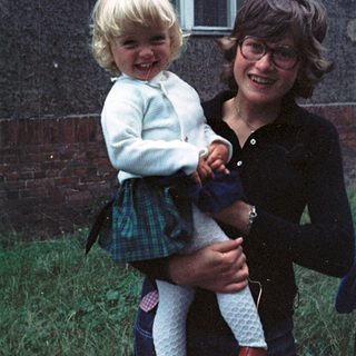 Joyful woman holding laughing young child outdoors.