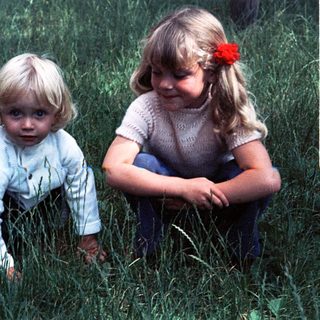 Two young children playing in tall grass.