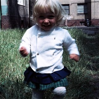 Joyful toddler running outdoors in grassy area.