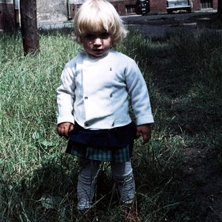 Young child standing outdoors in grassy area.